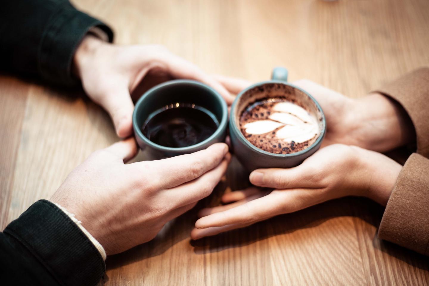 Hands of two people holding coffee cups on a table.